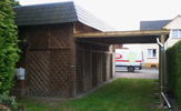 Carport mit einer Holz-Imprägnierung und Schieferverkleidung für einen Wohnwagen; seitlich zusätzlich ein einzelnes Carport
